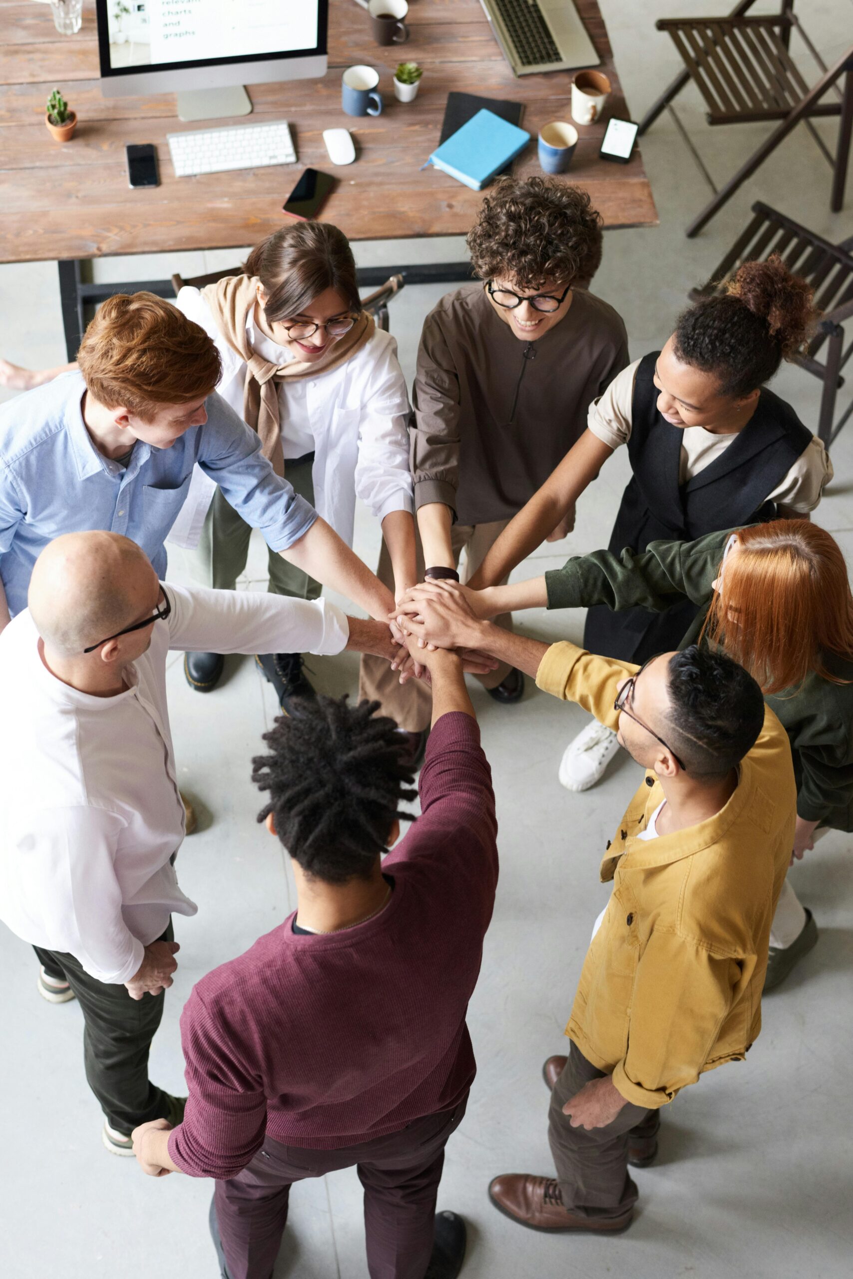 A diverse group of people standing in a circle with their hands stacked together in the center, symbolizing teamwork and unity.